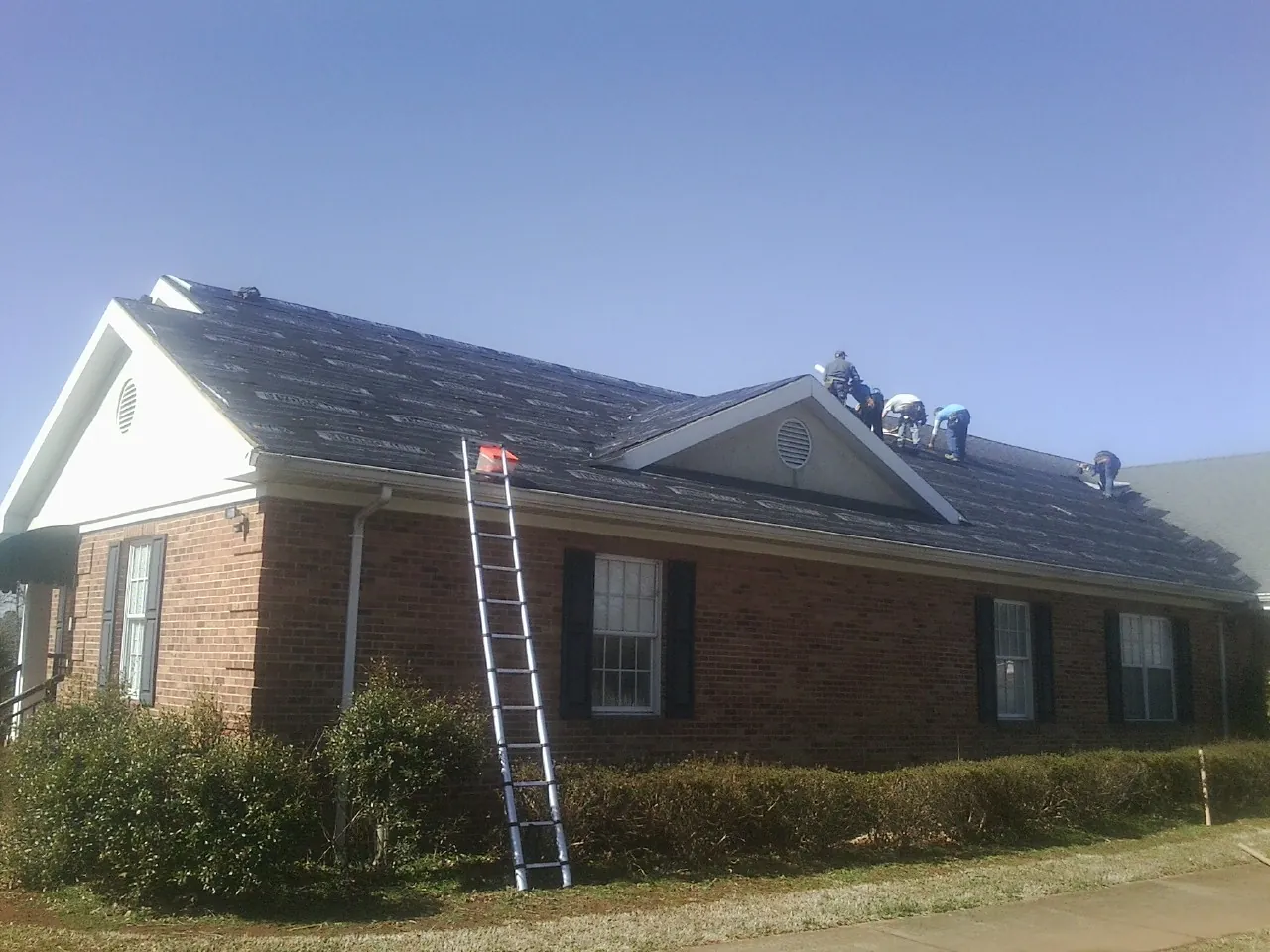 Crew tearing shingles off a brick ranch roof with a ladder set — Metal Roof Repair work by our crew in Mosheim