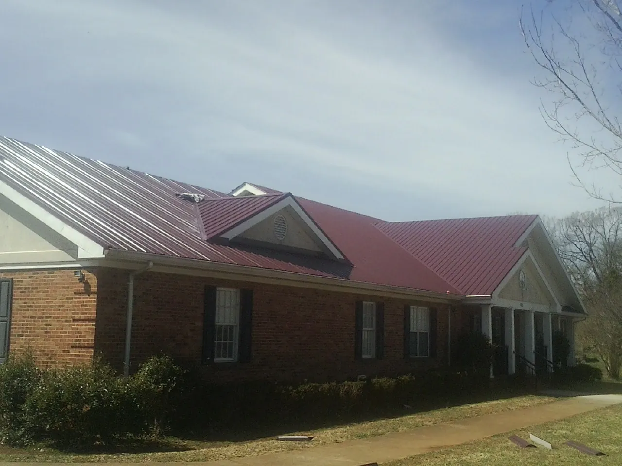 Red metal roof with gabled entries on a long brick building, from a Hail Damage Roof Repair job in Mosheim