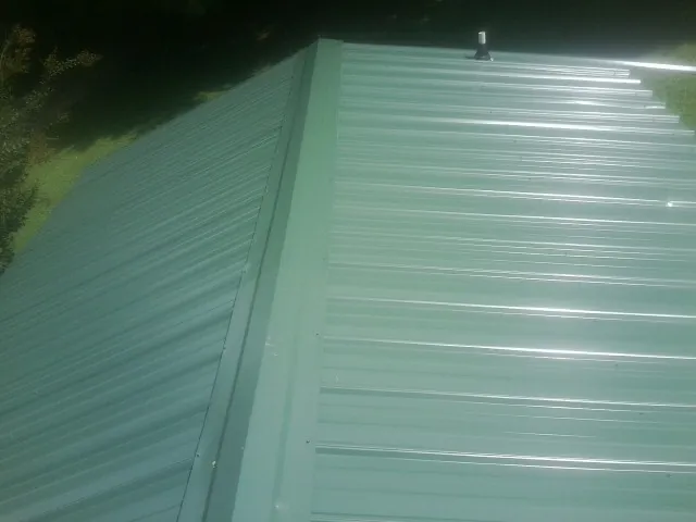 New green metal panels meeting at the ridge of a roof — Flat Roof Repair work by our crew in Mosheim