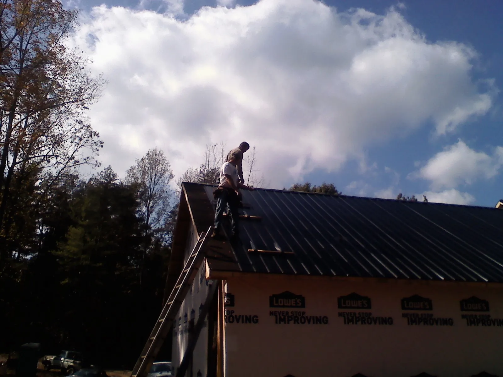 Roofer fastening dark metal panels high against a cloudy sky, from a Roof Inspection job in Mosheim