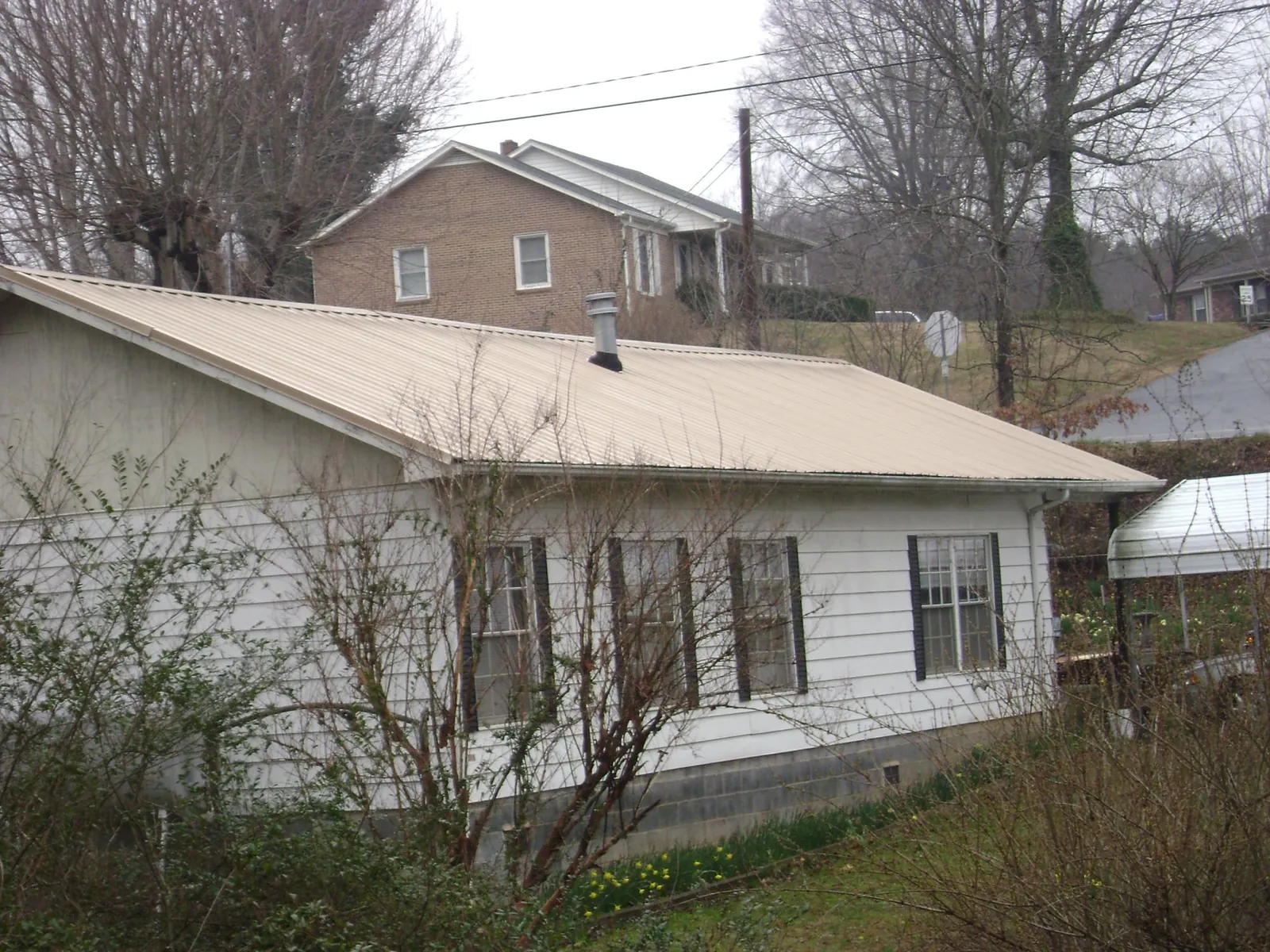 Tan metal roof on a white sided house set into a hillside — Commercial Roofing by Roofing Brothers in Mosheim