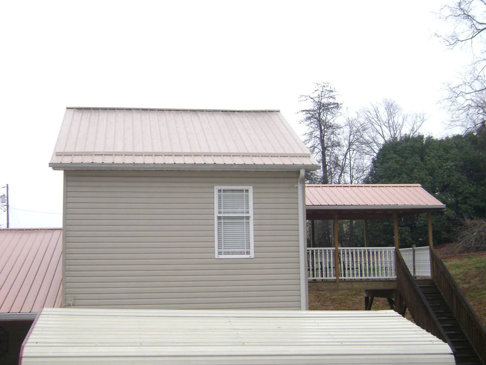 Tan metal roofs on a two story addition and attached porch, from a Roof Replacement job in Mosheim